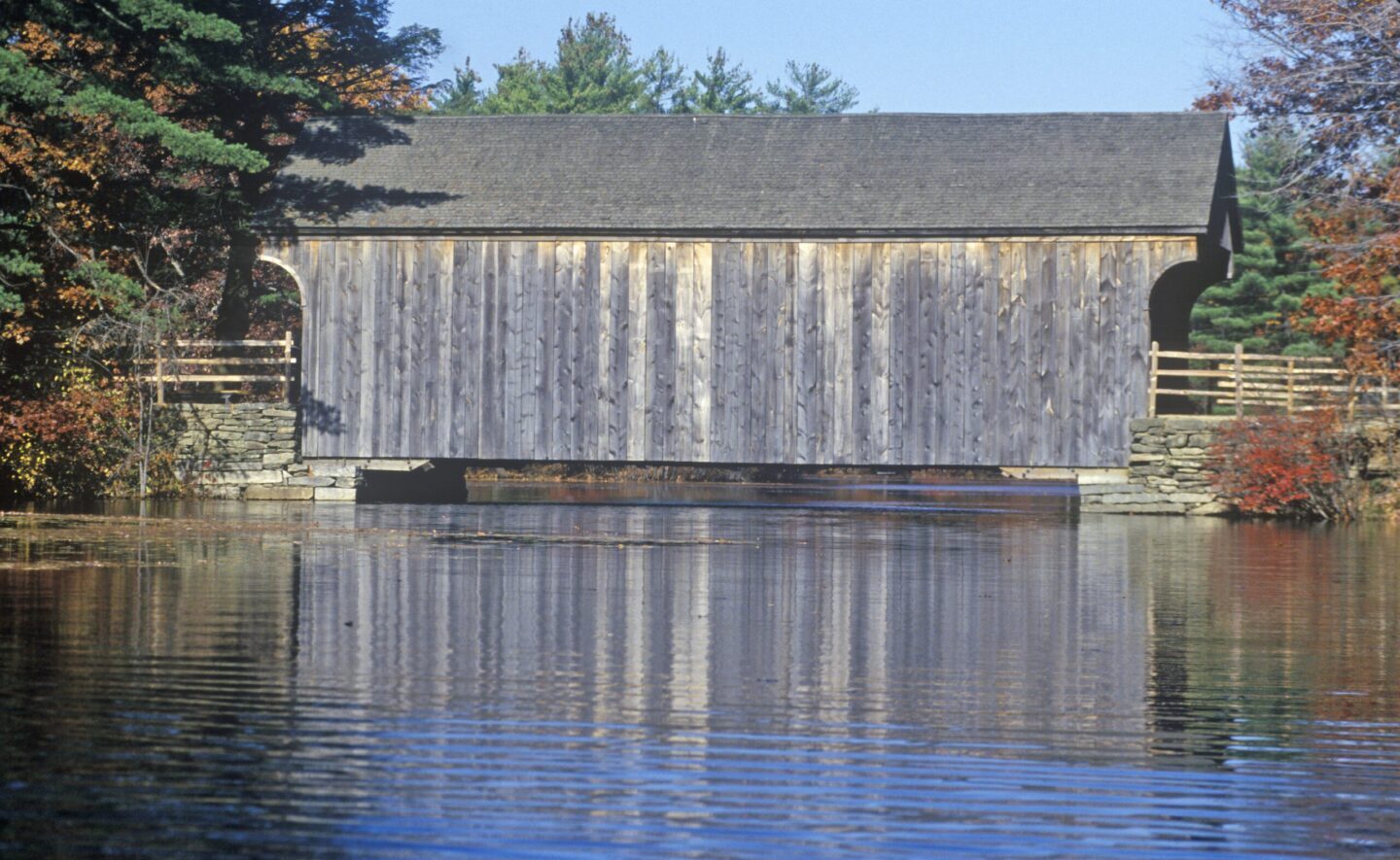 An old covered bridge in Sturbridge, Massachusetts, with a body of water in the foreground.