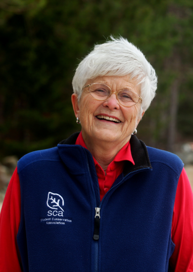 SCA Founder Liz Putnam in red shirt and navy SCA vest smiling outside