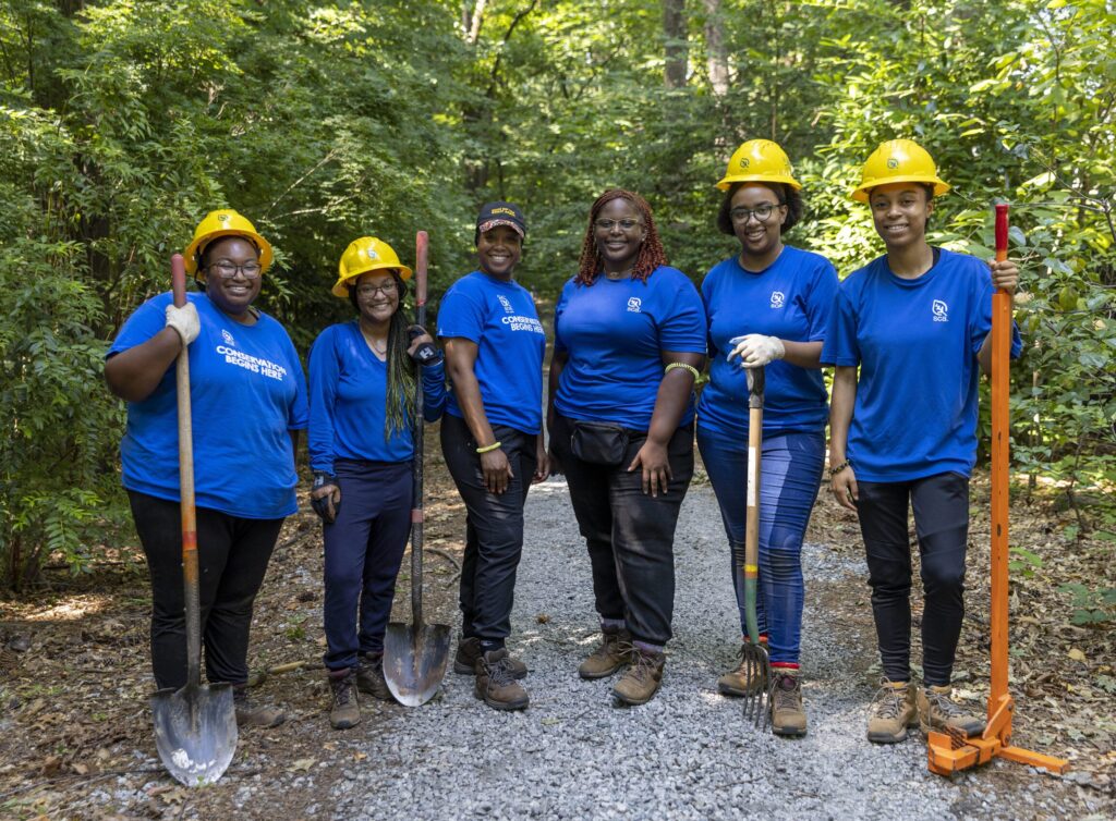 A group of youth crew members stand together to smile for the camera while working in the Atlanta Botanical Garden.