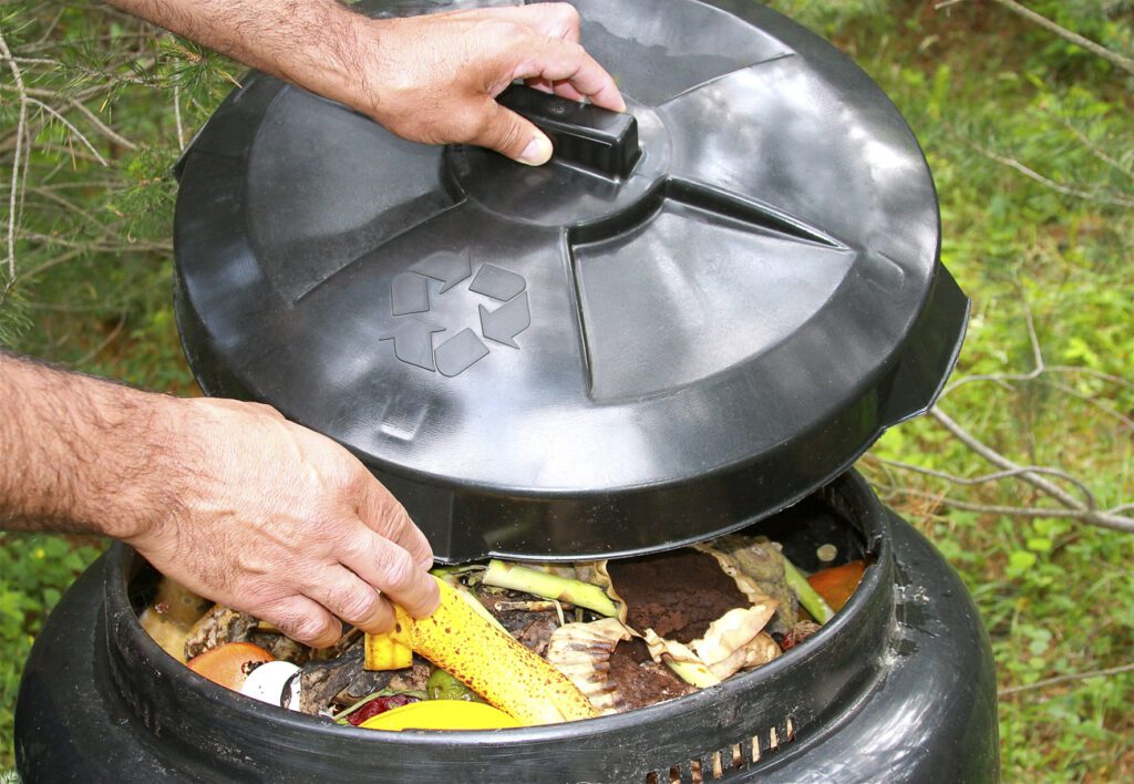 An individual places a banana peel in a backyard compost bin.