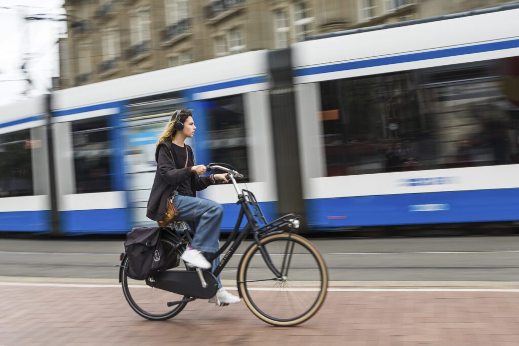 A commuter on a bicycle rides next to a public transit train. 