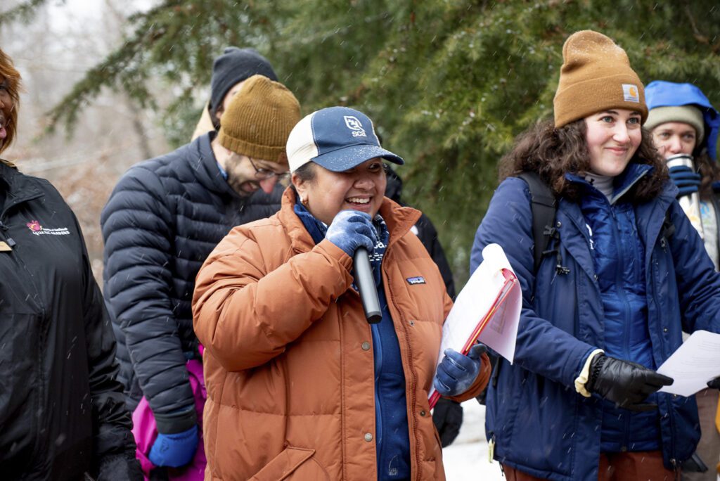 A group of SCA staff and crew members stand together. One person speaks into a microphone. 