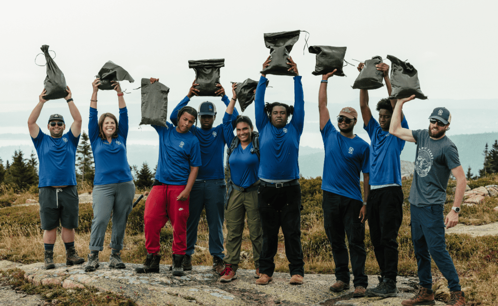 NY Urban Green Acadian Exploration Crew holding up bags of soil at the summit of Sargent Mountain at Acadia National Park in Maine.