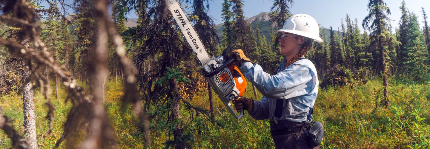 SCA Women's Fire Crew Member holding chain saw in forest.