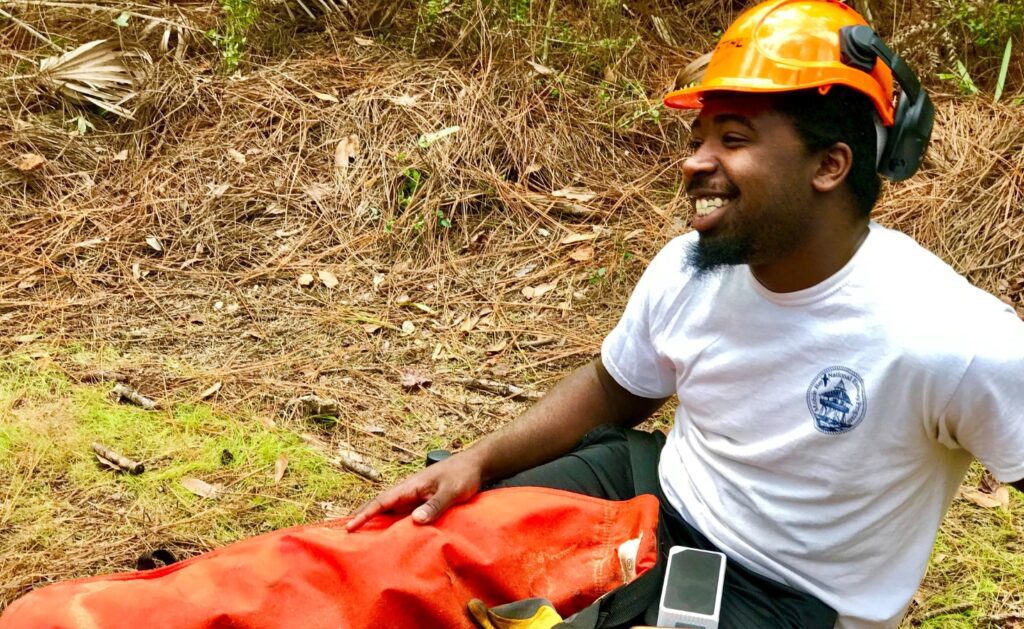 SCA Alum Eric Lucas sits on the ground smiling, taking a break from crew service.