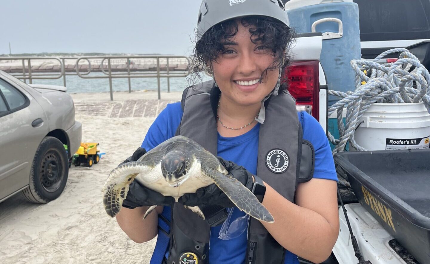 SCA alum Dora Figueroa wearing a helmet and bright blue SCA shirt, holds up a Kemp's ridley sea turtle.