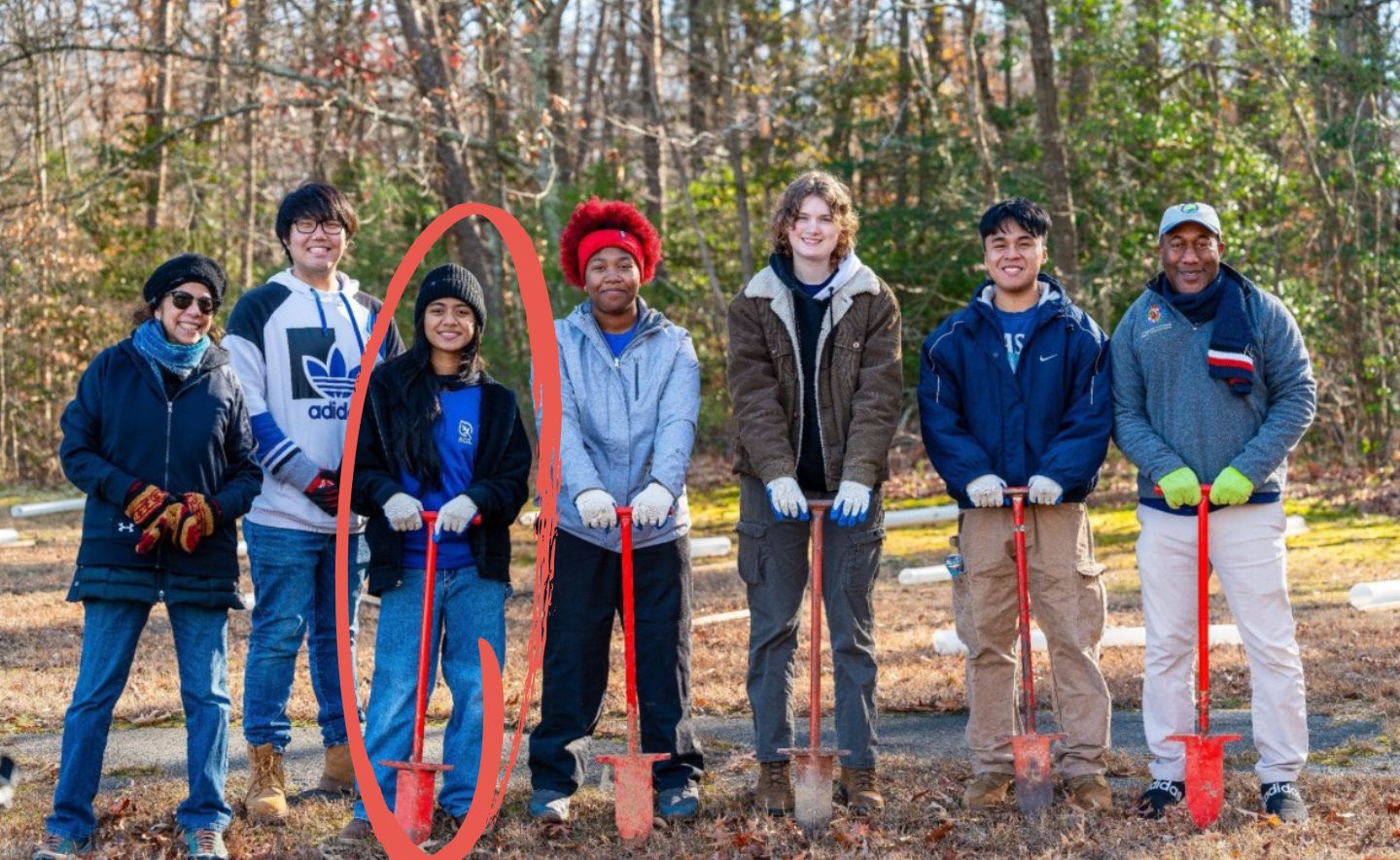 Group photo of crew members standing in a stright ling outdoors holding red shovels